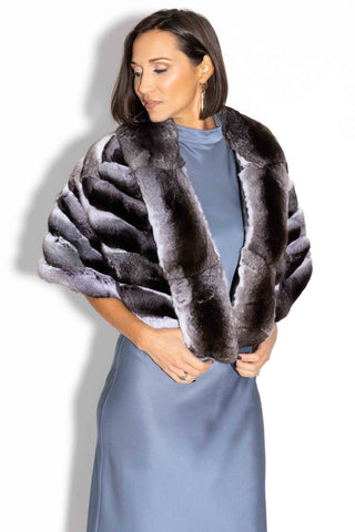 woman wearing a chinchilla fur cape against a white backdrop, looking down