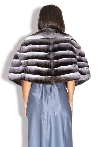 back of woman wearing a chinchilla fur cape against a white backdrop