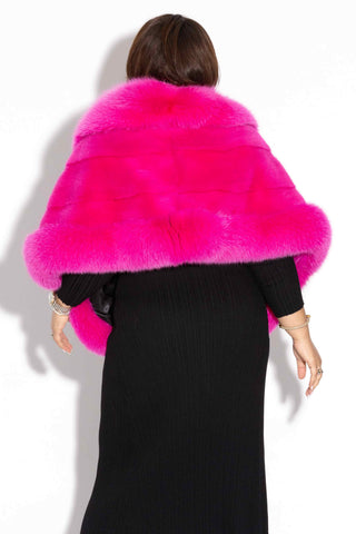 back of woman wearing a hot pink mink fur cape with fox fur trim against a white backdrop