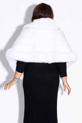 back of woman wearing a white mink fur cape with fox fur trim against a white backdrop