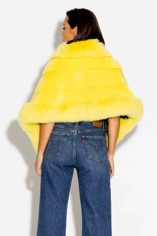 back of woman wearing a yellow mink fur cape with fox fur trim against a white backdrop