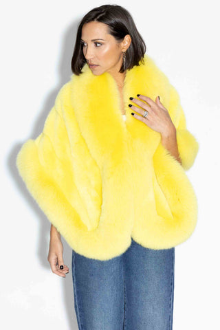 woman wearing a yellow mink fur cape with fox fur trim against a white backdrop
