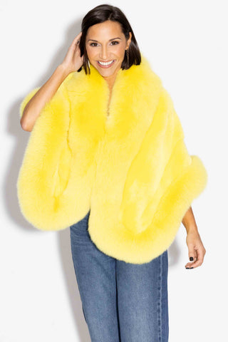 smiling woman wearing a yellow mink fur cape with fox fur trim against a white backdrop