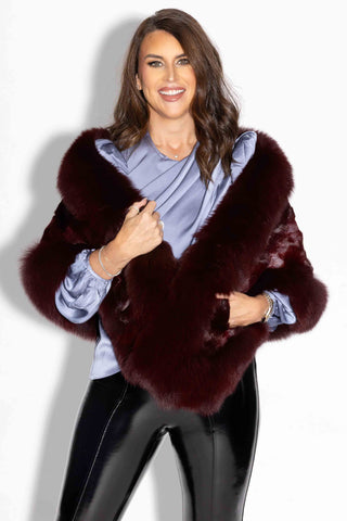 smiling woman wearing a burgundy chevron sectioned mink fur cape with fox fur trim against a white backdrop
