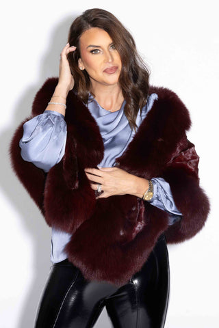 woman wearing a burgundy chevron sectioned mink fur cape with fox fur trim against a white background