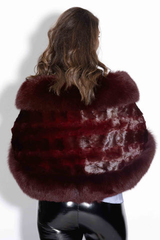 back of woman wearing a burgundy chevron mink fur cape with fox fur trim against a white backdrop
