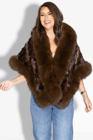 woman wearing a mahogany chevron sectioned mink fur cape with fox fur trim against a white backdrop