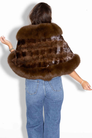 back of woman wearing a mahogany chevron sectioned mink fur cape with fox fur trim against a white backdrop
