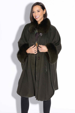 smiling woman wearing an olive cashmere & wool blend cape with fox fur trim against a white backdrop