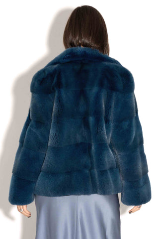 back of woman wearing a blue green mink fur jacket with horizontal pattern against a white backdrop