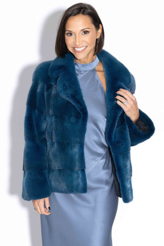 smiling woman wearing a blue green mink fur jacket with horizontal pattern against a white backdrop