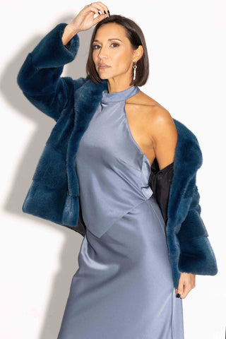 woman wearing a blue green mink fur jacket with horizontal pattern against a white backdrop