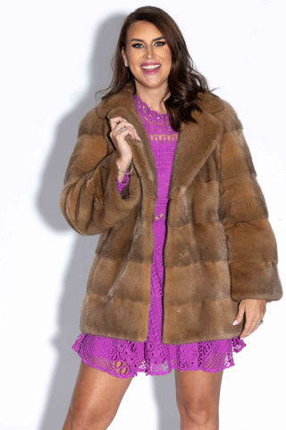 smiling woman wearing a camel mink fur jacket with horizontal pattern against a white backdrop
