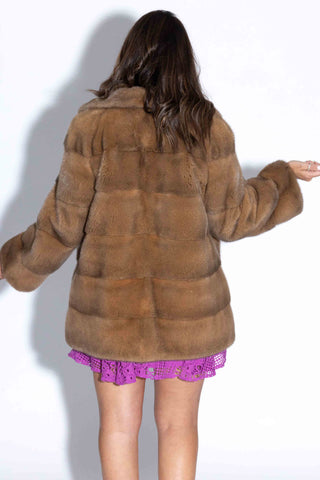 back of woman wearing a camel mink fur jacket with horizontal pattern against a white backdrop