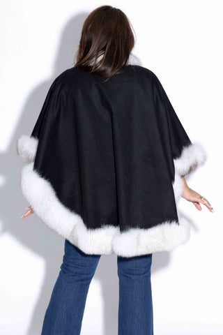back of woman wearing a black cashmere blend cape with white fox fur trim against a white backdrop