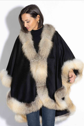 woman wearing a black cashmere blend cape with golden island fox fur trim against a white backdrop
