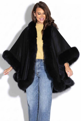 close view of smiling woman wearing a black cashmere blend cape with black fox fur trim against a white backdrop