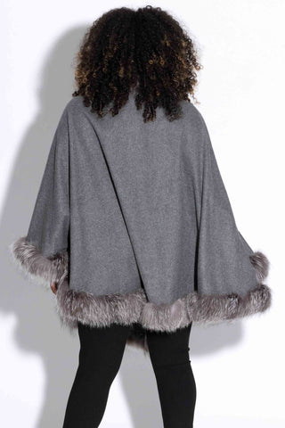 back of woman wearing a gray cashmere blend cape with silver fox fur trim against a white backdrop