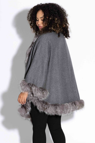 side profile of woman wearing a gray cashmere blend cape with silver fox fur trim against a white backdrop