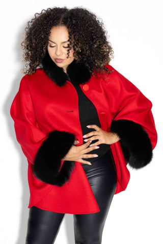 woman wearing a red cashmere & wool blend cape with black fox fur trim against a white backdrop
