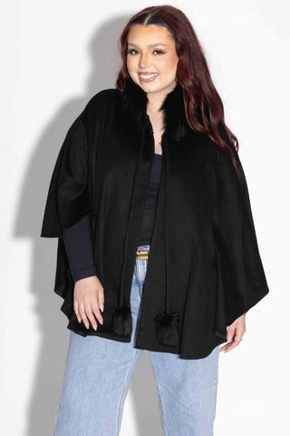 smiling woman wearing a black wool blend cape with fox fur trim against a white backdrop