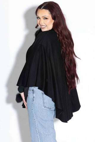 side profile of woman wearing a black wool blend cape with fox fur trim against a white backdrop