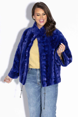 smiling woman wearing a royal blue sheared sectioned mink fur capelet against a white backdrop