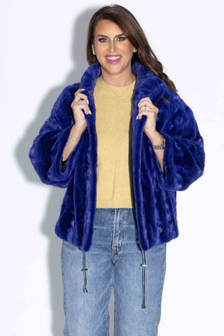 smiling woman wearing a royal blue sheared sectioned mink fur capelet against a white backdrop