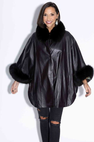 smiling woman wearing a black leather capelet with fox fur trim against a white backdrop