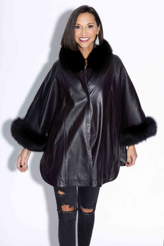 smiling woman wearing a black leather capelet with fox fur trim against a white backdrop