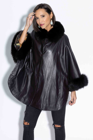 3/4 profile of woman wearing a black leather capelet with fox fur trim against a white backdrop