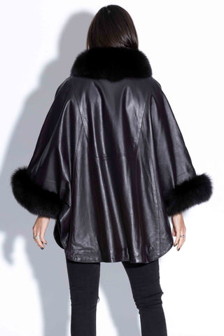 back of woman wearing a black leather capelet with fox fur trim against a white backdrop
