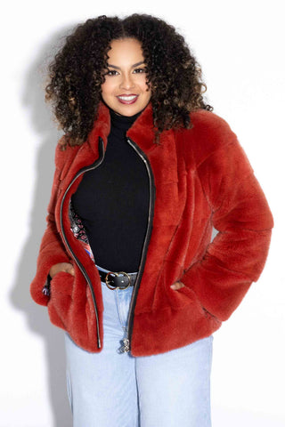 woman wearing a paprika mink fur jacket with horizontal pattern and zip front, with her hands in the pockets, against a white backdrop