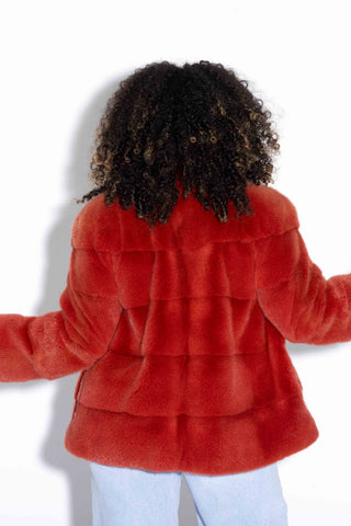 back of woman wearing a paprika mink fur jacket with horizontal pattern and zip front against a white backdrop