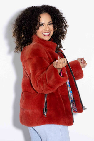 smiling woman wearing a paprika mink fur jacket against a white backdrop
