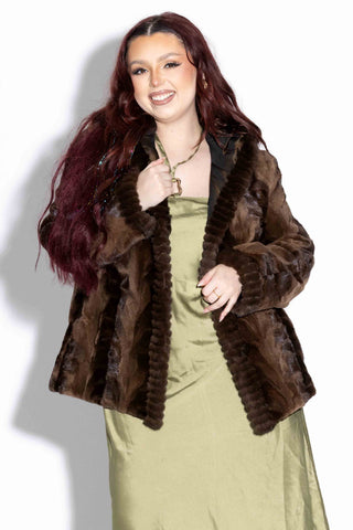 smiling woman wearing a brown Reversible Sheared Sectioned Mink Fur Jacket with Hood against a white backdrop