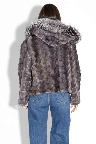 back of woman wearing a blue iris chevron sectioned mink fur jacket with silver fox fur trimmed hood