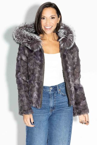 smiling lady wearing a blue iris chevron sectioned mink fur jacket with silver fox fur trimmed hood against a white backdrop