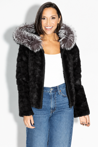 smiling woman wearing a ranch chevron sectioned mink fur jacket with silver fox fur trimmed hood against a white backdrop