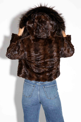 back of woman wearing a brown chevron sectioned mink fur jacket with fox fur trimmed hood against a white backdrop, with the hood up