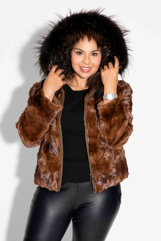 woman wearing a whisky chevron sectioned mink fur jacket with a brown fox fur trimmed hood against a white backdrop