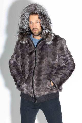 man wearing a reversible blue iris sectioned mink fur bomber jacket with silver fox fur trimmed hood up, standing against a white backdrop