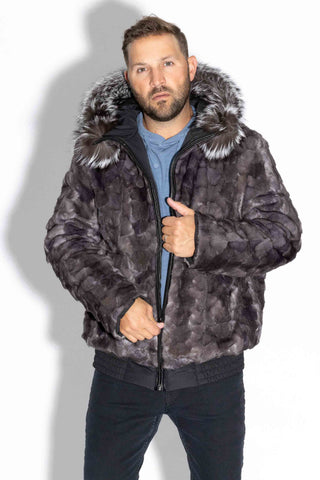 man wearing a reversible blue iris sectioned mink fur bomber jacket with silver fox fur trimmed hood against a white backdrop