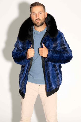 man wearing a reversible blue cross sectioned mink fur bomber jacket with black fox fur trimmed hood against a white backdrop