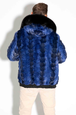 back of a man wearing a reversible blue cross sectioned mink fur bomber jacket with black fox fur trimmed hood against a white backdrop