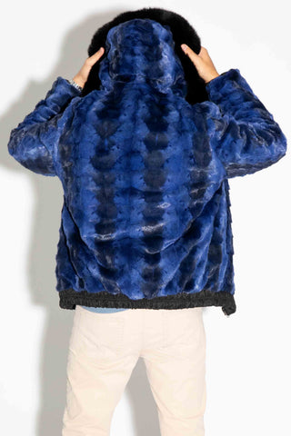 back of a man wearing a reversible blue cross sectioned mink fur bomber jacket with black fox fur trimmed hood up, standing against a white backdrop