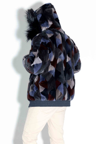 side profile of man wearing a reversible blue multicolor sectioned mink fur bomber jacket with navy fox fur trimmed hood against a white backdrop