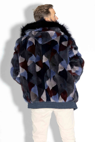 back of man wearing a reversible blue multicolor sectioned mink fur bomber jacket with navy fox fur trimmed hood against a white backdrop