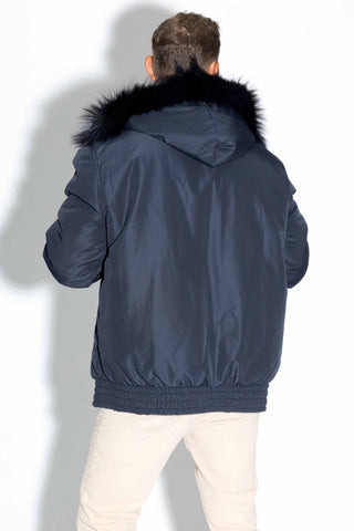back of man wearing a reversible blue multicolor sectioned mink fur bomber jacket with navy fox fur trimmed hood, with the navy cloth side facing out, against a white backdrop