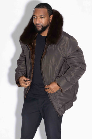 man wearing a brown reversible sectioned mink fur bomber jacket with brown fox fur trimmed hood, with brown cloth side facing out, against a white backdrop